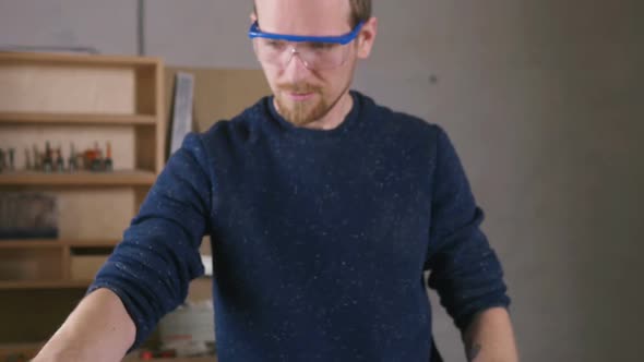 Young Man Working As Carpenter and Put Eye Protection Glasses on Slow Motion alt