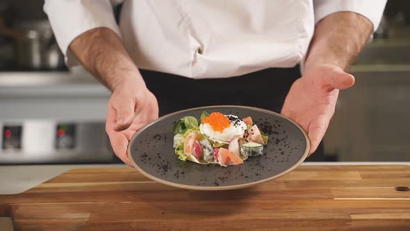 He Chef Serves a Salad of Lightly Salted Salmon with Poached Egg and Red Caviar on a Black Plate