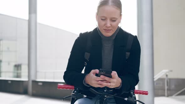 Woamn leaning on bicycle, text messaging on smart phone alt