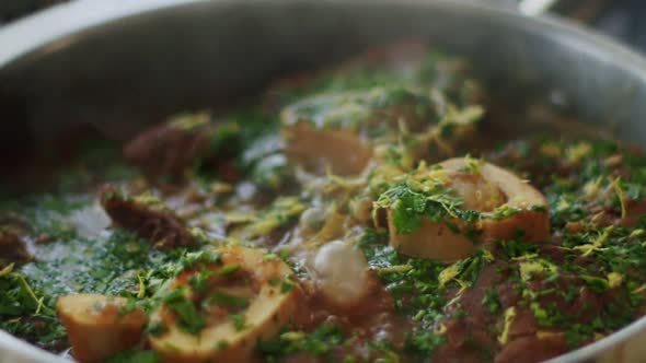 Woman adding lemon zest to stewing ossobuco alt