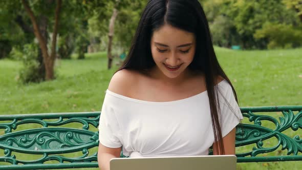 Young Asian woman using laptop at a public park.