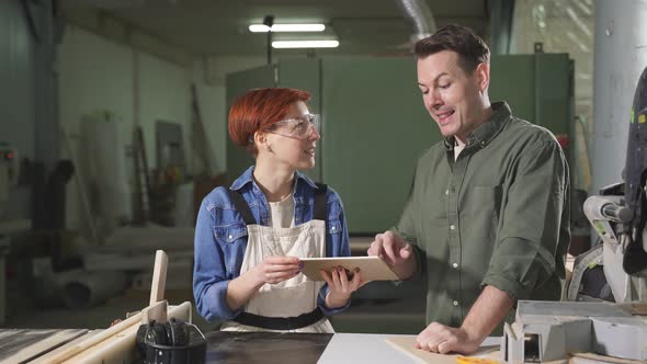 Young Caucasian Man and Woman Joiners Using Digital Tablet While Working in Workshop