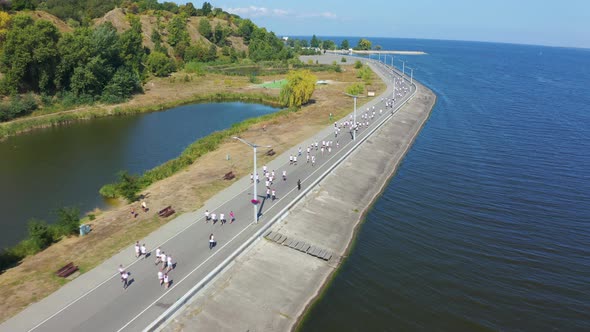 Marathon Runners in White T-shirts Running Along the Promenade. Aerial View Footage alt