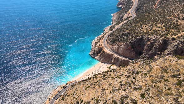 Flying a drone along the coastal strip of a green mountain over a mountain road, driving cars to the alt