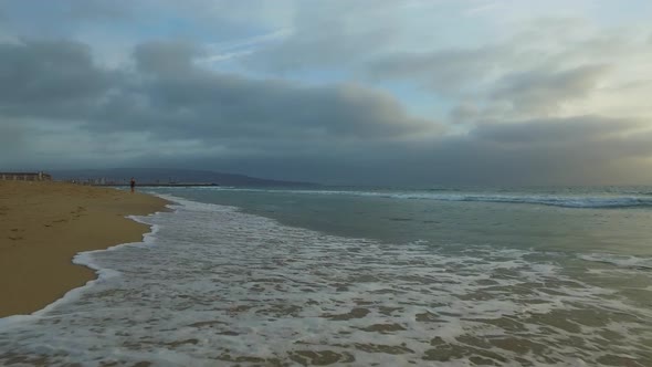 Tracking shot of the ocean waves, beach and pier at sunset. alt