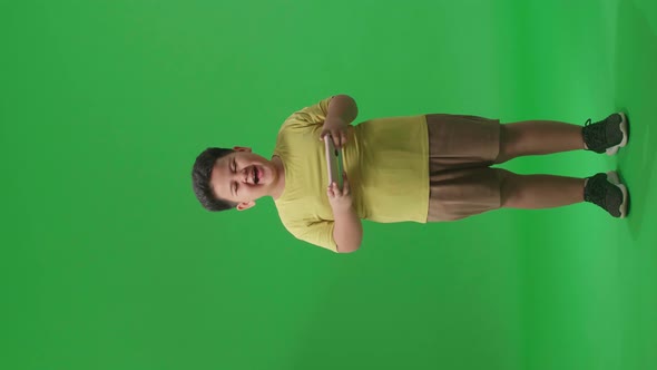Full Body Of Laughing Asian Little Boy Looking At The Phone On Green Screen In The Studio alt
