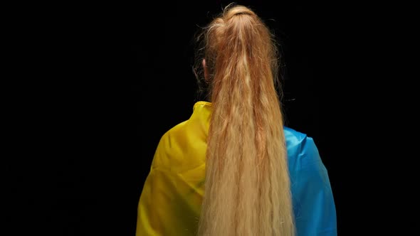 Back View Woman in Ukrainian Flag Standing at Black Background Turning Looking at Camera with alt