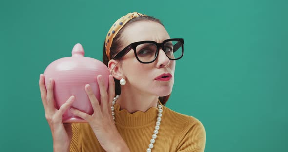 Funny sixties style woman shaking a money box checking her savings, looking perplexed. Isolated.