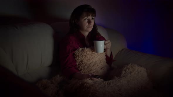 Woman Relax on the Couch and Watches Tv in the Evening Worries Drinks Coffee Watching Tv with