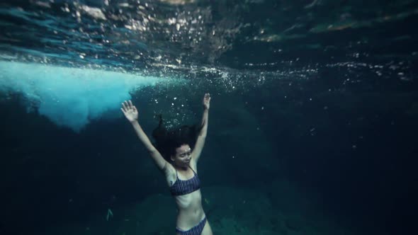 A Young Skinny Woman in Bikini Floating Underwater and Holding Her Breath alt