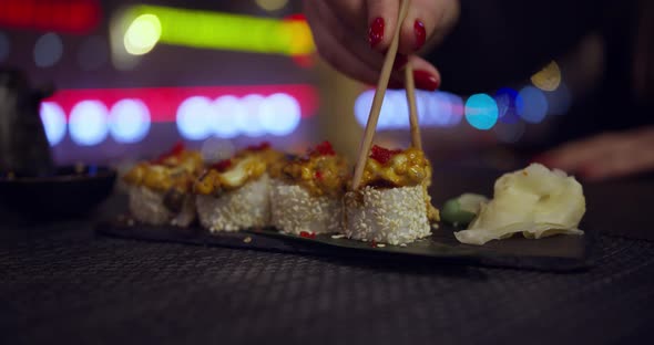 Woman Takes Sushi Sticks in a Traditional Japanese Restaurant with a View of the Night City