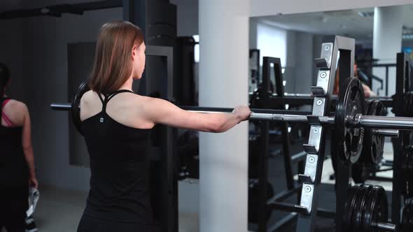 Athletic Young Woman Walks Up to the Weight Bar and Lifts Her in the Fitness Club  alt