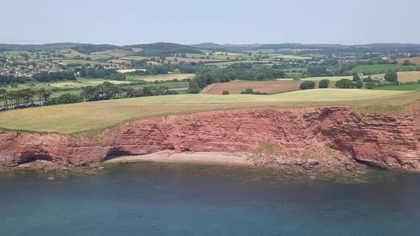 Aerial DOLLY ZOOM of red cliffs along the Jurassic Coast and Devon countryside alt