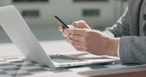 Closeup of Male Hands Who is Working on Laptop and Scrolling the Smartphone alt