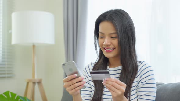 Asian attractive woman enjoy shopping online in living room at home. alt
