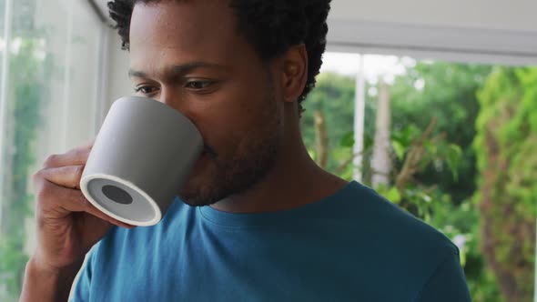 Relaxed biracial man drinking coffee, smiling and looking into distance alt