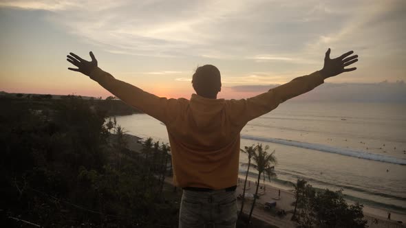 Young Man Traveler Raising His Hands High on Top of the Big Mountain Above the Ocean and Beautiful