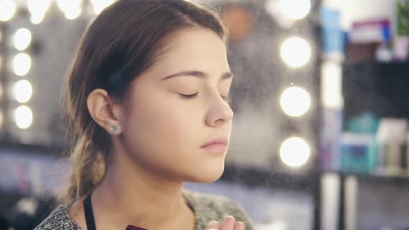 Professional Makeup Artist Fixing Young Woman's Makeup with Spray in a Beauty Salon alt