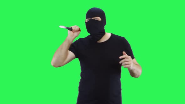 A man in a black mask holds in his hand a knife goes forward.Balaclava.Green screen background.
