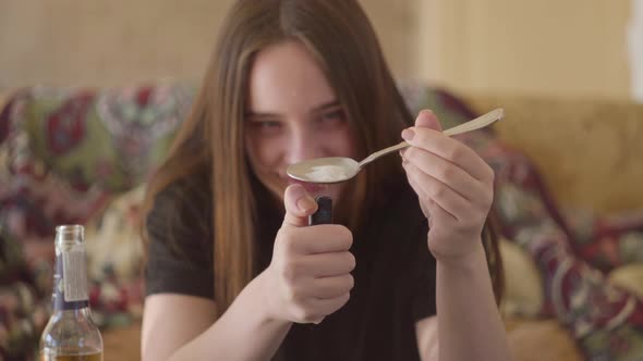 Young Smiling Woman with Long Hair Warming a Spoon with Heroin on a Lighter Fire Close-up. Drug Use alt