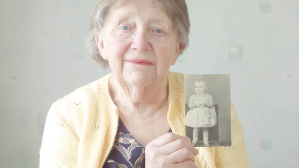 Senior Woman Holding up an Old Photograph of Herself