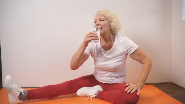 Woman in Sportswear Sits on a Fitness Mat and Drinks Water After Yoga and Fitness Classes at Home