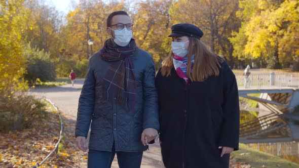 Happy Couple Wearing Protective Mask Holding Hands Walking in Autumn Park