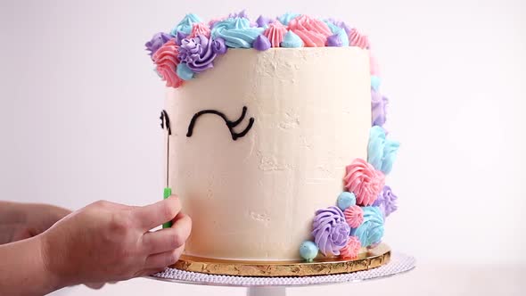 Piping unicorn eyes with a black buttercream icing on a white cake. alt