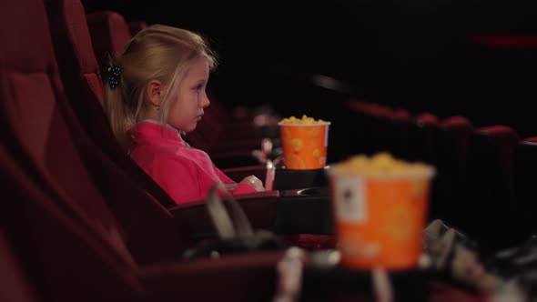 Little Girl Alone in the Cinema Looks at the Cinema Screen alt