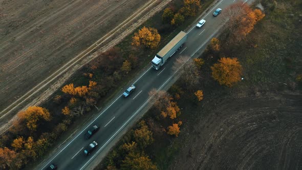Aerial View of a Truck Driving in a Flow of Cars Along the Highway at Autumn Sunset alt