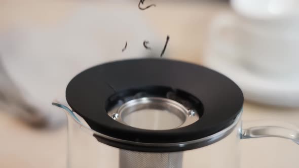 pouring fragrant dried tea leaves into a glass teapot. jar close-up. alt