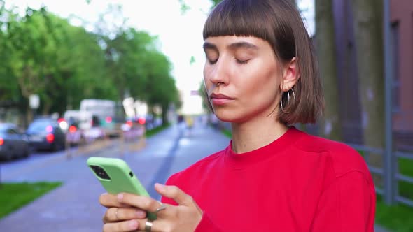 Stylish Girl Messaging on Phone on Urban Street with Traffic Jam on Background alt