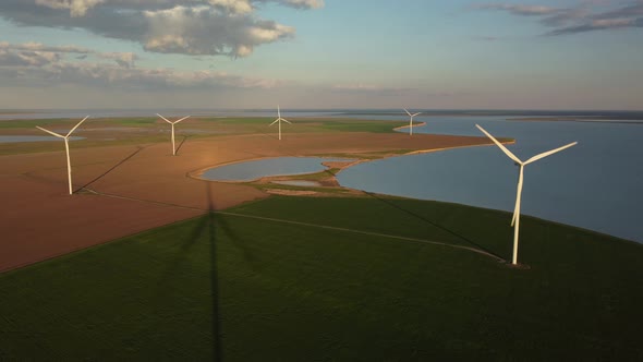 Aerial View of Wind Turbines and Agriculture Field Near the Sea at Sunset alt