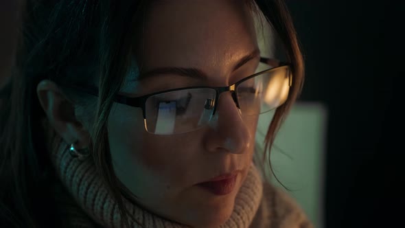 Pretty woman in eyeglasses late at night scrolling with smartphone