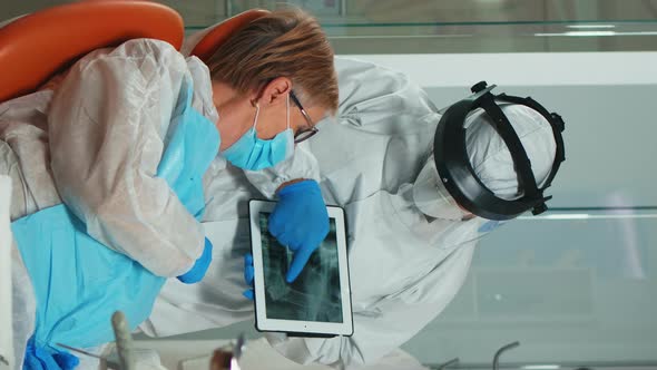 Vertical Video Stomatologist in Protective Suit Reviewing Xray of Tooth Using Tablet alt