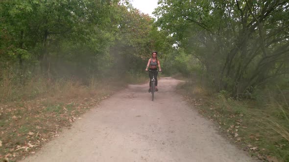 Aerial Slow Motion Shot of Young Sport Woman Rides Bicycle on Countryside Dusty Road at Summer alt