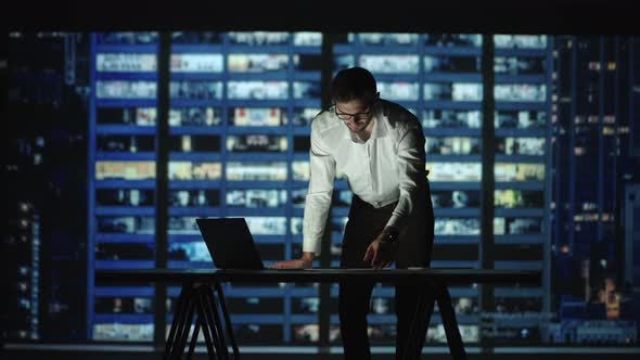 A Bearded Arab Man in Glasses and a Shirt Against the Backdrop of the Night City Stands at the alt