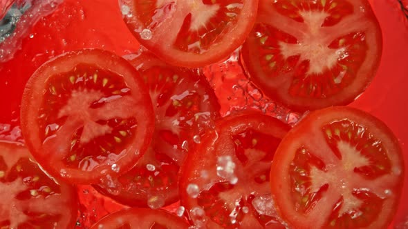 Super Slow Motion Shot of Tomato Slices Falling Into Water on Red Background at 1000Fps. alt