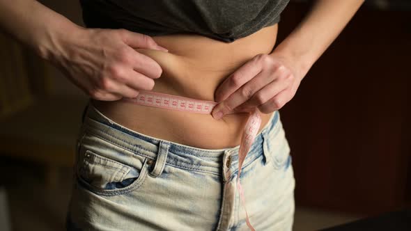 A young woman measures her obese belly next to a half-eaten pizza alt