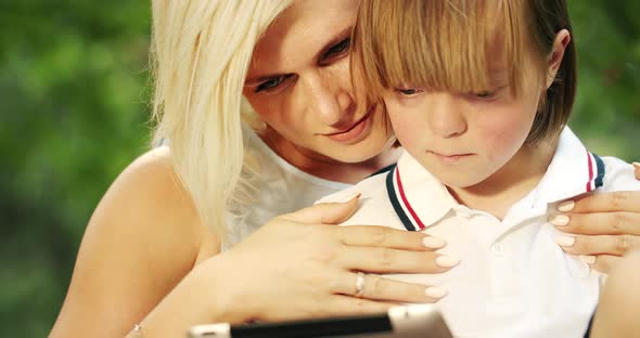 Down Syndrome Boy Holding Tablet with Mother