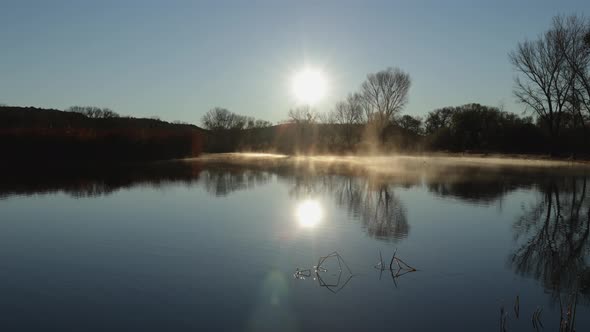 Fog Slowly Rolls Across a Lake at Sunrise alt