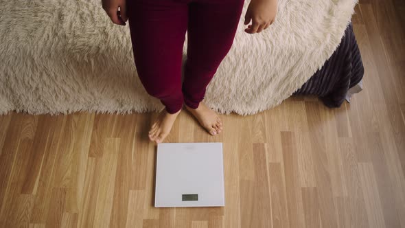 Woman in Burgundy Trousers Stands on a Floor Scale Barefoot to Measure the Weight alt