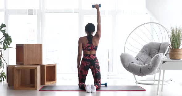 Fitness black woman doing arm workout with dumbbells in room. alt