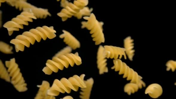 Closeup of the Dry Pasta Fusili Flying Diagonally on a Black Background alt