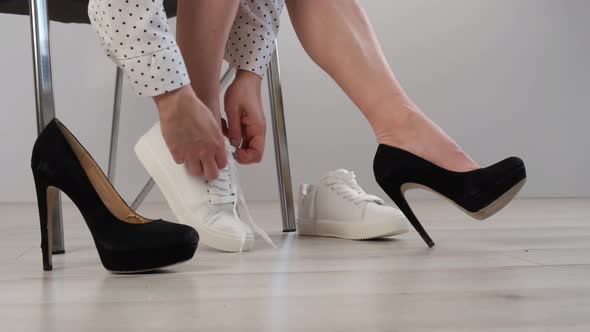 Business Woman Takes Off White Leather Sneakers and Puts on Black High Heel Shoes alt