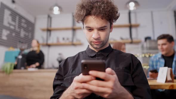 Young Concentrated Middle Eastern Man with Curly Hair and Brown Eyes Messaging Online Using Social alt