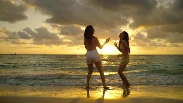Two beautiful Asian women are having fun dancing on the beach at sunset