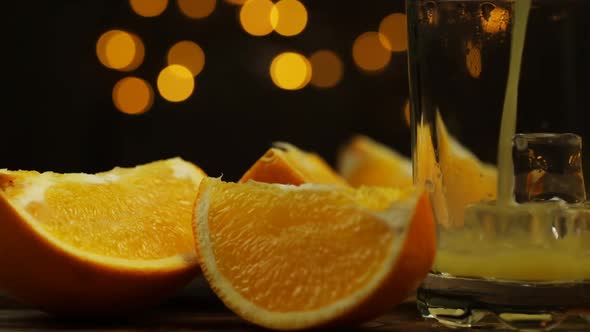 Orange Juice Is Poured Into A Glass And Slices Of Oranges With Lights On The Background