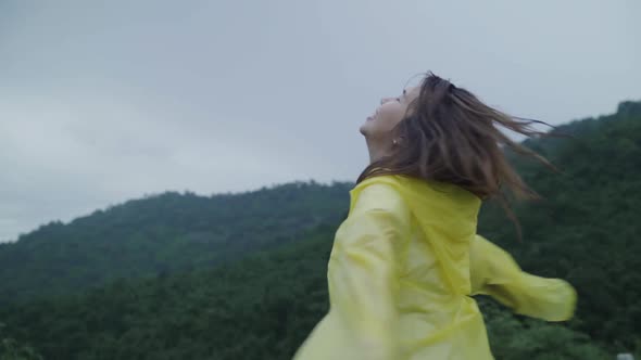Young Asian woman feeling happy playing rain while wearing raincoat standing near lake. alt
