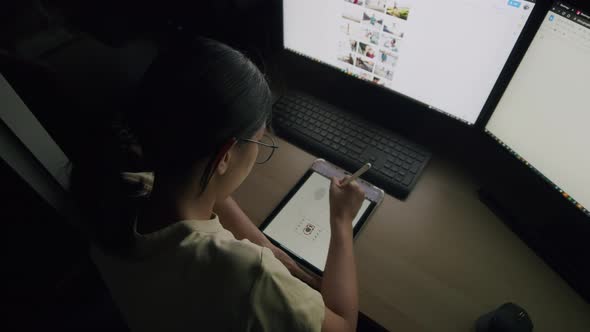 Young Asian drawing her work on a tablet at night in a home office.